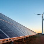 Solar panels and a wind turbine on an Australian renewable energy site at dusk, photographed from ground level with golden side lighting.